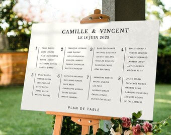 May include: A white wedding seating chart with black text on an easel. The chart lists the names of guests and their assigned tables for a wedding reception. The text at the top reads "Camille & Vincent Le 18 Juin 2023" and "Plan de Table".