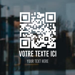 May include: White QR code with the text "VOTRE TEXTE ICI" above "YOUR TEXT HERE" on a glass surface. The background is blurred, suggesting an indoor or outdoor setting.