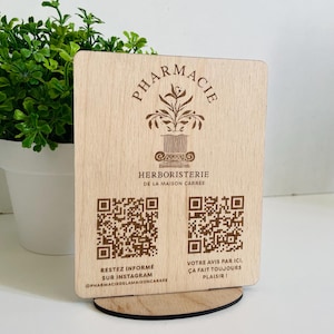 May include: A wooden sign with the text "Pharmacie Herboristerie de la Maison Carree" and two QR codes. The text "Restez informe sur Instagram @pharmaciedlamaisoncarree" and "Votre avis par ici, ca fait toujours plaisir!" is also included.