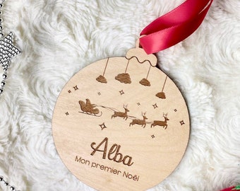 Könnte beinhalten: Weihnachtsbaumschmuck aus Holz mit rotem Band. Der Schmuck zeigt ein lasergraviertes Design von Santa in einem Schlitten, der von Rentieren, Wolken und Sternen gezogen wird. Der Name "Alba" und "Mon premier Noël" sind ebenfalls eingraviert.