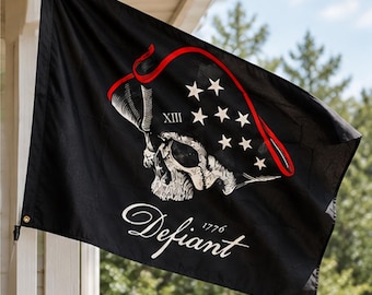 May include: A black rectangular flag featuring a white skull wearing a tricorn hat adorned with white stars and a red trim. The Roman numeral XIII is visible on the hat. Below the skull, the word Defiant and the year 1776 are printed in white.