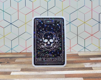 May include: A white card with a black background and a white skull with flowers around it. The card says "The Plant Lover" at the bottom.