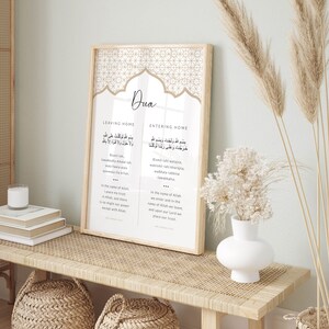 K&ouml;nnte beinhalten: Ein gerahmter Druck mit beigefarbenem Hintergrund und einem geometrischen Muster. Der Druck zeigt das Wort "Dua" in einer dekorativen Schriftart und zwei Spalten Text in Arabisch und Englisch. Der Text handelt vom Verlassen und Betreten eines Hauses mit einem Gebet im Namen Allahs.