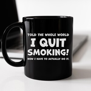 以下が含まれることがあります： 白い文字で「TOLD THE WHOLE WORLD I QUIT SMOKING! NOW I HAVE TO ACTUALLY DO IT.」と書かれた黒いコーヒーカップ