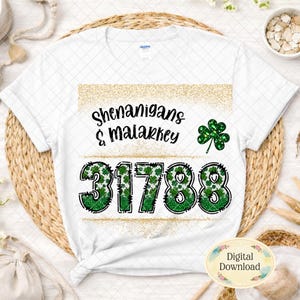 Może przedstawiać: Biała koszulka z czarnym napisem "Shenanigans & Malarkey", zieloną koniczyną i cyframi "31788" w kolorze zielonym z wzorami koniczyny. Koszulka ma złoty brokatowy wzór.