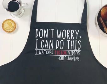 May include: Black kitchen apron with white text that reads "Don't worry, I can do this. I watched TikTok videos -Chef Janine"