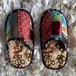 May include: A pair of patchwork fabric slippers with a floral design. The slippers are quilted and have a black trim.