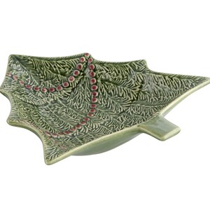 May include: Green ceramic Christmas tree-shaped serving dish with a textured surface. The dish features a decorative pattern of red bead-like accents. The tree-shaped dish is a festive addition to holiday decor.