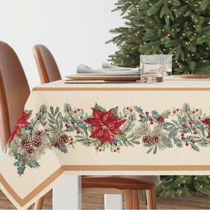Op de afbeelding: Een crèmekleurige tafelkleed met een gouden rand heeft een herhalend patroon van kerststerren, dennentakken, bessen en dennenappels. Het tafelkleed ligt op een tafel met twee stoelen.