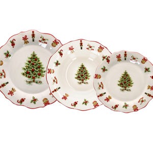Puede incluir: Un juego de tres platos de cerámica blanca con bordes rojos festoneados, cada uno con un árbol de Navidad verde central con adornos rojos y un patrón de borde de cascanueces, caballitos de madera, campanas y acebo con lazos rojos.