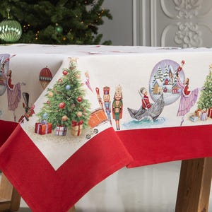 Puede incluir: Un mantel blanco con un borde rojo presenta una escena navideña festiva con un tema de Cascanueces. El mantel representa un árbol de Navidad, un soldado Cascanueces, una bailarina y un pueblo de invierno.
