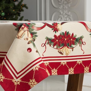 Könnte beinhalten: Weihnachtstischdecke mit cremefarbenem Hintergrund und rotem Rand. Das Design zeigt rote Weihnachtssternblumen, Glocken und Bänder. Der Rand hat ein Schneeflockenmuster.