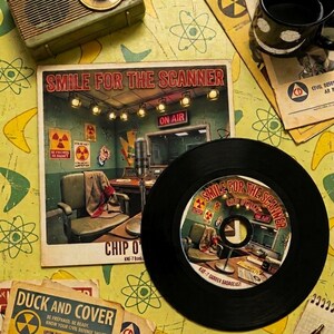 Puede incluir: Un disco de vinilo y su funda cuadrada de cartón titulada Smile for the Scanner de Chip O'Toole. La ilustración muestra un estudio de radio con un micrófono, una silla y señales de advertencia de radiación. La etiqueta del disco repite el título.
