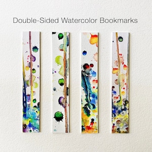 May include: Four double-sided watercolour bookmarks with abstract designs. Each bookmark has a vertical stripe of paint with splatters of blue, green, yellow, red, and purple. The text "Double-Sided Watercolor Bookmarks" is at the top.