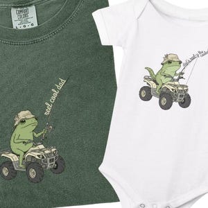 May include: A dark green t-shirt and a white baby onesie. Both feature a cartoon frog wearing a hat and fishing from an ATV. The shirt has the text "reel cool dad". The onesie has the text "that's really the coolest".