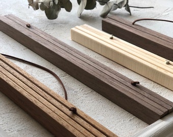 May include: Three wooden hanging picture frames in different shades of brown, with a light brown, a dark brown, and a natural wood finish. Each frame has a string attached for hanging.