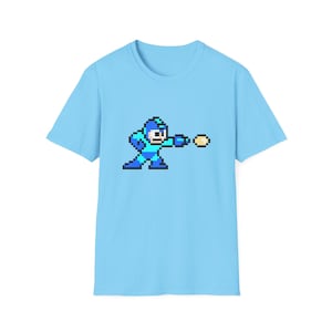 May include: A light blue t-shirt with a pixelated image of a blue and green video game character shooting a yellow projectile.