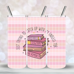 May include: A pink and white checkered tumbler with the text "Just trying to catch up with my endless TBR" and a stack of books with the titles "Fated Mates", "Slow Burn", and "Dark Romance".