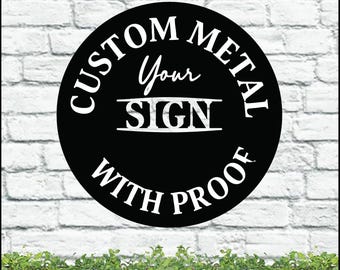 Pode incluir: Uma placa de metal preta com texto branco que diz "CUSTOM METAL Your SIGN WITH PROOF" em um design circular. A placa está colocada contra uma parede de tijolos brancos com uma floreira de madeira cheia de plantas verdes na parte inferior.