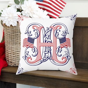 May include: White throw pillow with a red, white, and blue decorative letter H in a blue and red floral design. The letter H is surrounded by two small American flags.