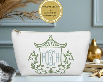 May include: A white zippered pouch featuring a green pagoda-style graphic with a central light blue monogram of the letters MGH, surrounded by green scrollwork. The pouch has a gold zipper pull and a clean, minimalist aesthetic design.