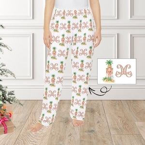 May include: White pajama pants with a repeating pattern of a nutcracker with a palm tree and the letter "M". The nutcracker is pink and green. The pants are loose-fitting and have an elastic waistband.