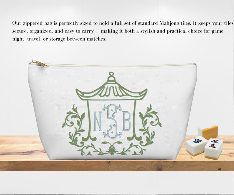 May include: White zippered bag with a green and blue decorative design. The bag features a gold zipper and is designed to hold Mahjong tiles. The bag is on a wooden surface with Mahjong tiles.