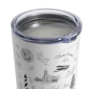 May include: White stainless steel tumbler with a black and white design featuring various North Carolina landmarks, including the state seal, a lighthouse, a building, and an aeroplane. The text "North Carolina" is visible on the tumbler.
