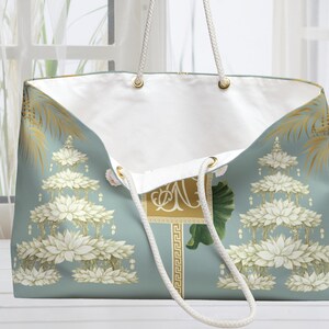 May include: A large tote bag with a light blue background and a white interior. The bag features a floral design with gold accents and white rope handles. The bag has a rectangular gold emblem with the letter "N".