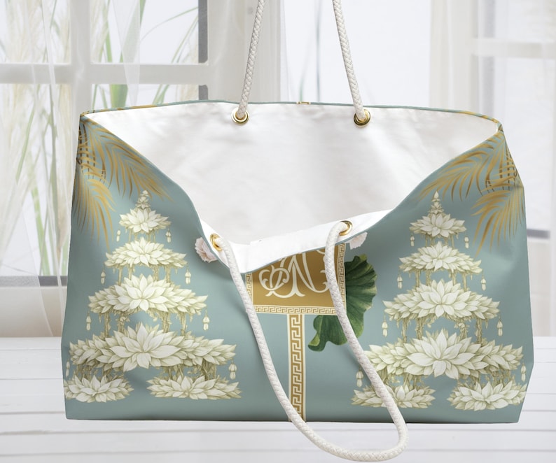 May include: A large tote bag with a light blue background and a white interior. The bag features a floral design with gold accents and white rope handles. The bag has a rectangular gold emblem with the letter "N".