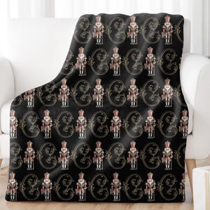 May include: Black and gold throw blanket with a repeating pattern of nutcracker figurines and ornate scrollwork.