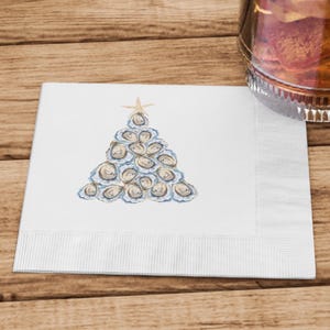 May include: White paper napkin with a watercolor illustration of a Christmas tree made of oyster shells. The tree is topped with a gold star.