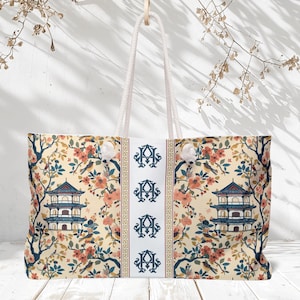 May include: A large tote bag with a cream-colored background featuring a repeating pattern of a pagoda, birds, and flowering branches in shades of blue, coral, and brown. The bag has white rope handles and a central panel with monogrammed initials.