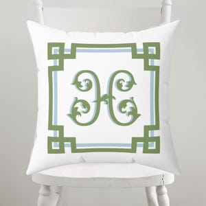 Peut inclure: Coussin carr&eacute; blanc avec un motif d&eacute;coratif vert et bleu clair. Le coussin pr&eacute;sente la lettre "H" verte au centre, entour&eacute;e d'une bordure verte et bleu clair. Le coussin est pos&eacute; sur une chaise blanche.