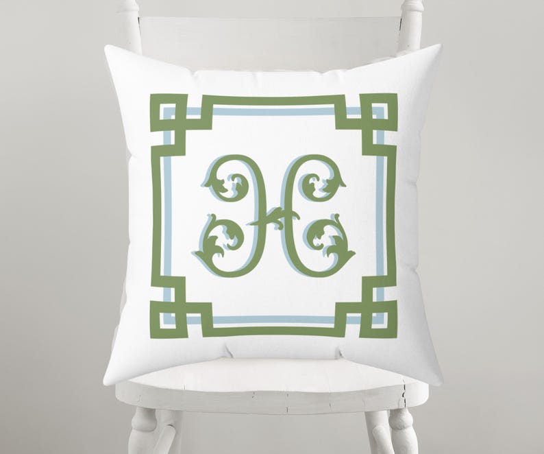 Peut inclure: Coussin carr&eacute; blanc avec un motif d&eacute;coratif vert et bleu clair. Le coussin pr&eacute;sente la lettre "H" verte au centre, entour&eacute;e d'une bordure verte et bleu clair. Le coussin est pos&eacute; sur une chaise blanche.
