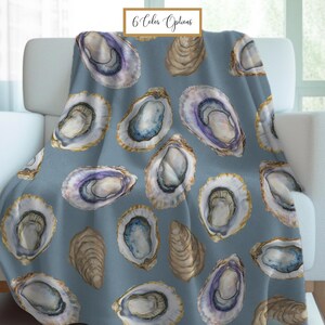 May include: A blue throw blanket with a repeating pattern of oyster shell illustrations in shades of white, purple, and gold. The blanket is draped over a white armchair. The text "6 Color Options" is in the upper left corner.