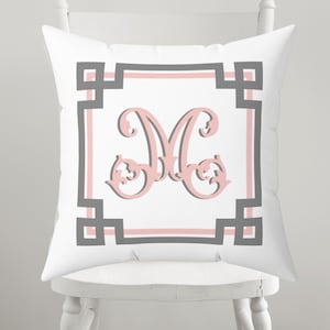 May include: White square throw pillow featuring a large, ornate pink letter "M" within a gray and pink geometric border. The pillow is on a white chair, showcasing a decorative home accent.