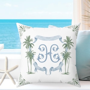 May include: White square throw pillow with a watercolor design featuring palm trees, a blue banner, and ornate scrollwork. The pillow has a blue monogram in the center. A starfish is in the foreground.