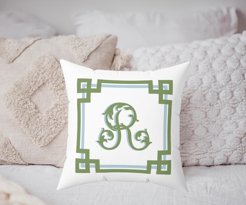 Peut inclure: Coussin carr&eacute; blanc avec une bordure verte et bleue et un &laquo; R &raquo; d&eacute;coratif vert au centre. Le coussin est pos&eacute; sur une surface blanche avec d'autres coussins d&eacute;coratifs en arri&egrave;re-plan.