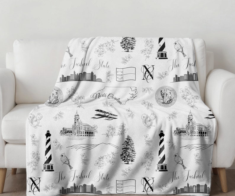 Peut inclure: Jet&eacute; de canap&eacute; noir et blanc avec un motif r&eacute;p&eacute;t&eacute; de monuments de Caroline du Nord, notamment le b&acirc;timent du Capitole de l'&Eacute;tat, un phare et le drapeau de l'&Eacute;tat. Le texte "The Tarheel State" est r&eacute;p&eacute;t&eacute; dans tout le motif.