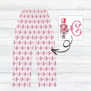May include: White leggings with a repeating pattern of pink nutcracker soldiers and the letter "C". A watercolor illustration of a pink nutcracker soldier and the letter "C" is in the upper right corner. The leggings are on a white wooden surface.