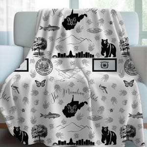 May include: Black and white throw blanket featuring a repeating pattern of West Virginia state symbols, including the state outline, the state seal, and the words "The Mountain State".