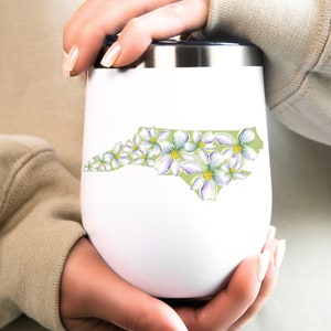 May include: White stainless steel tumbler with a green outline of the state of North Carolina, decorated with white flowers.