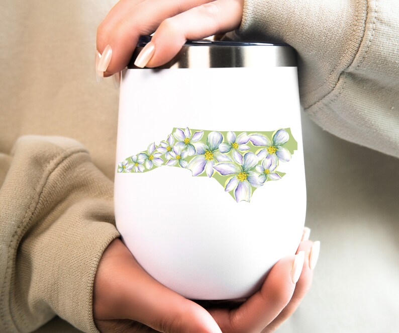 May include: White stainless steel tumbler with a green outline of the state of North Carolina, decorated with white flowers.