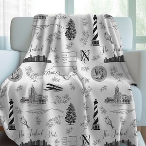 Peut inclure: Jet&eacute; de lit noir et blanc avec un motif r&eacute;p&eacute;t&eacute; de monuments de Caroline du Nord, notamment un phare, un drapeau d'&Eacute;tat et le texte "The Tarheel State".