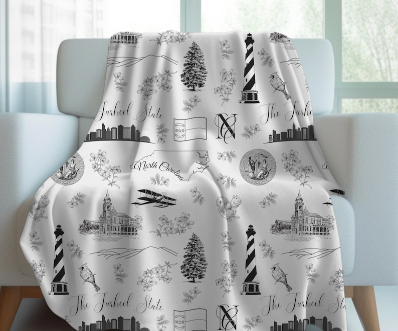 Peut inclure: Jet&eacute; de lit noir et blanc avec un motif r&eacute;p&eacute;t&eacute; de monuments de Caroline du Nord, notamment un phare, un drapeau d'&Eacute;tat et le texte "The Tarheel State".