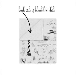 Peut inclure: Une couverture en polaire blanche avec un motif noir et blanc repr&eacute;sentant un phare, un oiseau et le texte "The Tarheel State". Le dos de la couverture est blanc.