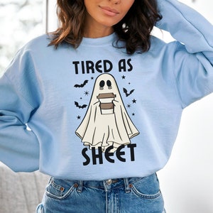 Peut inclure: Un sweat-shirt bleu clair avec un graphique d'un fantôme tenant une tasse de café et le texte "TIRED AS SHEET".