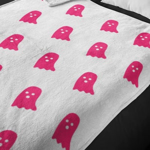 Puede incluir: Manta de forro polar blanca con un patr&oacute;n de fantasmas rosas.
