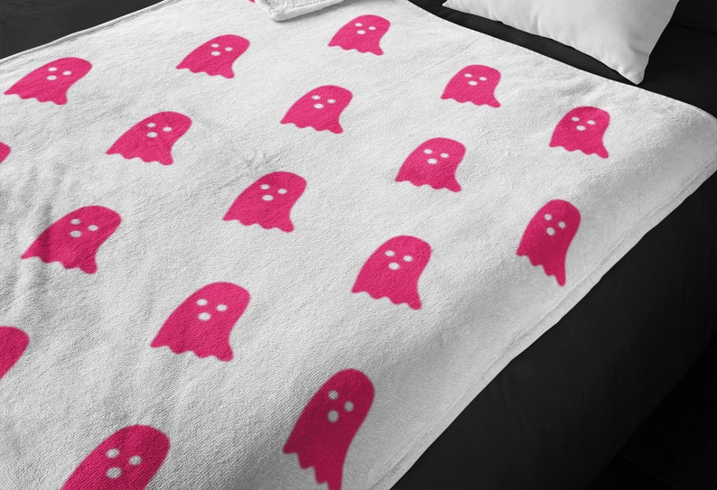 Puede incluir: Manta de forro polar blanca con un patr&oacute;n de fantasmas rosas.